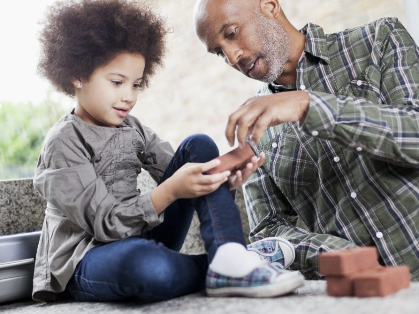 A man and a small girl playing with "mini bricks". Man is wearing a checkered shirt, girl with curly hair sitting next to him.