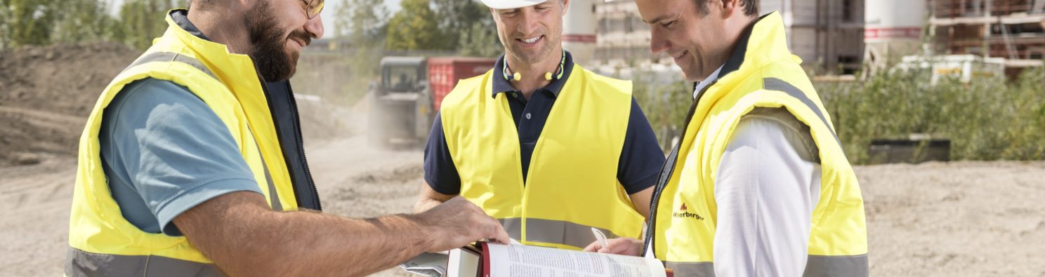 Three building professionals at construction site looking at documents