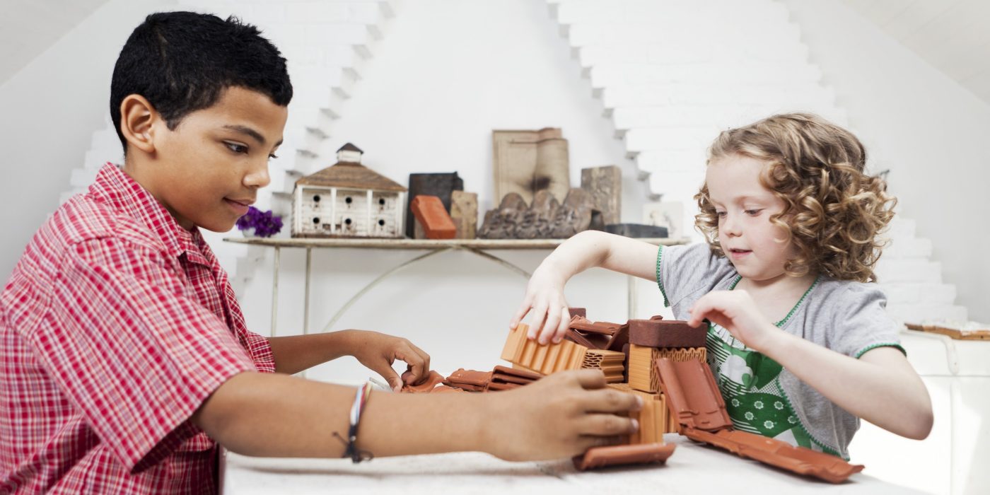 Boy and girl playing with miniature bricks, clay blocks and clay roof tiles in attic loft