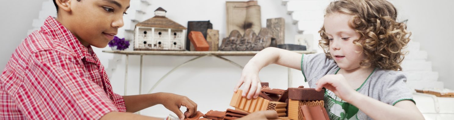 Boy and girl playing with miniature bricks, clay blocks and clay roof tiles in attic loft