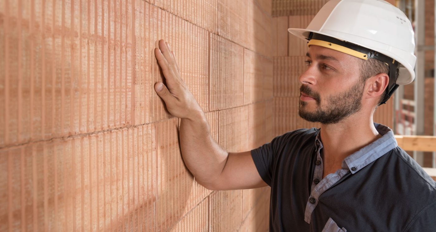 Man with white helmet puts hand on brick wall