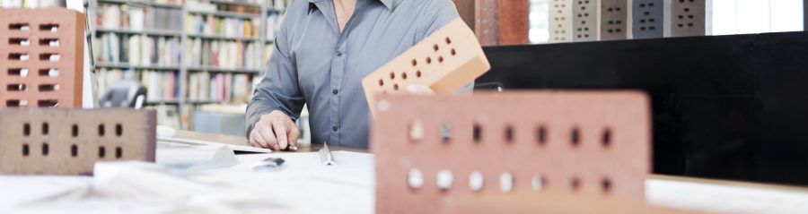 Architect at his office sitting at desk with blueprint surrounded by bricks