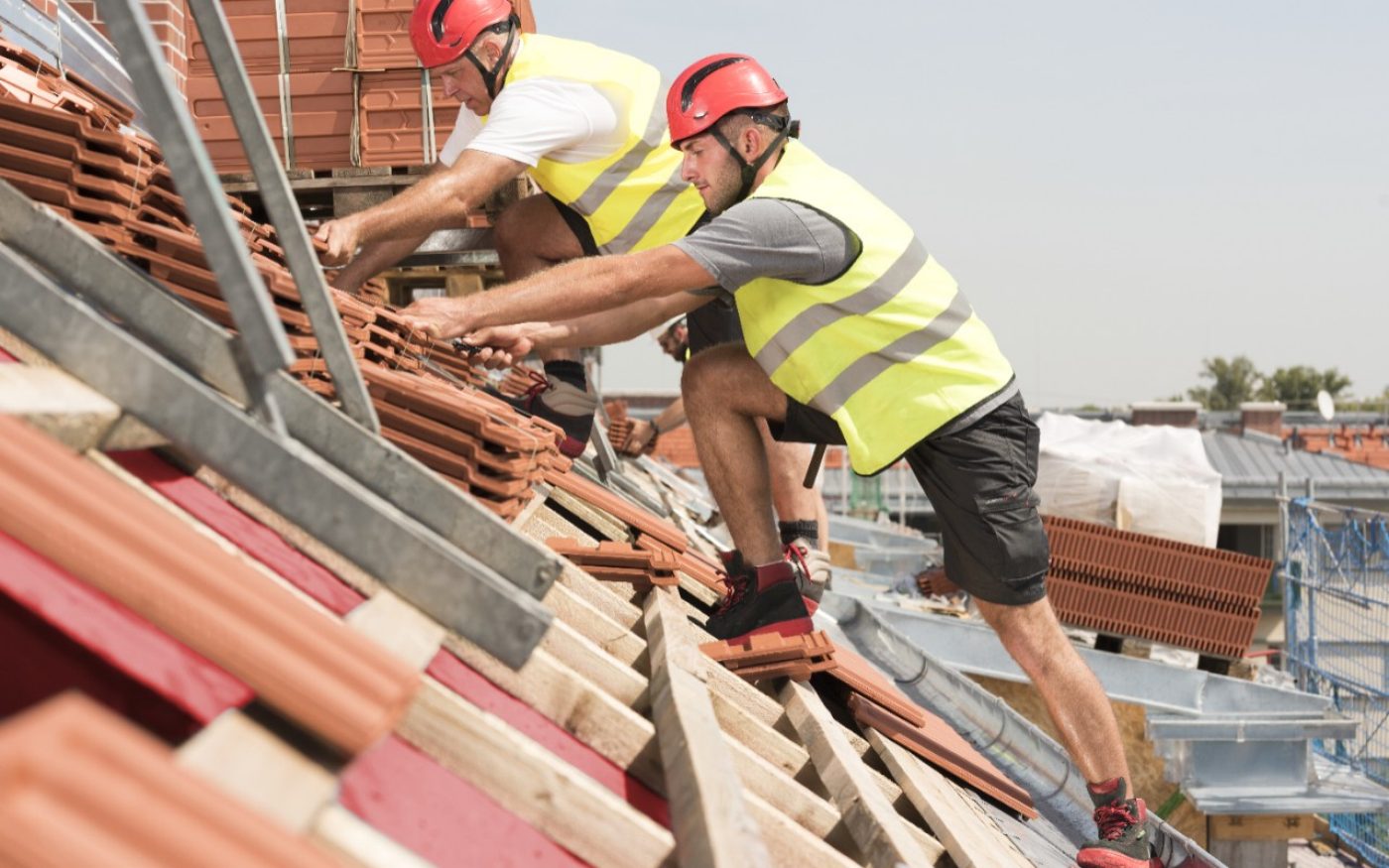 Urban roofers at work wearing safety jackets and hard hats laying roof tiles