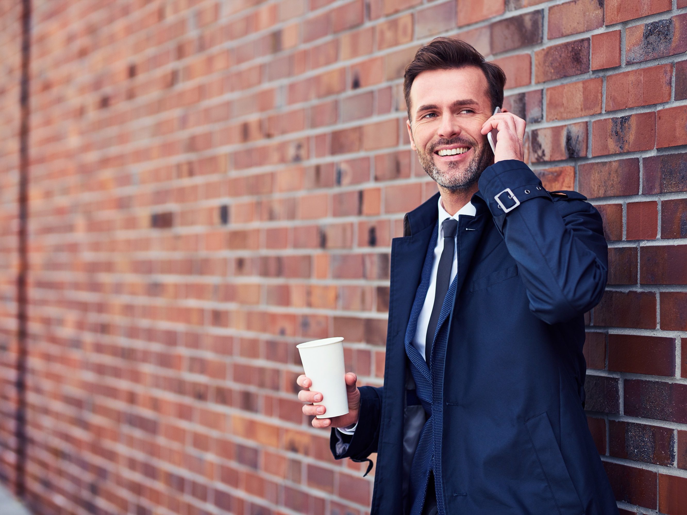 Middle-aged business executive making phone call while enjoying a cup of coffee outside