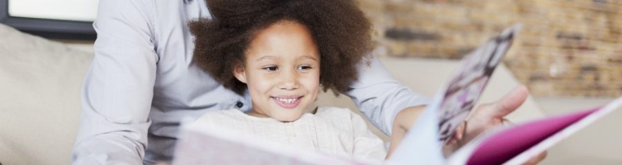 Smiling man and young kid flipping through a book sitting on sofa in front of brick wall