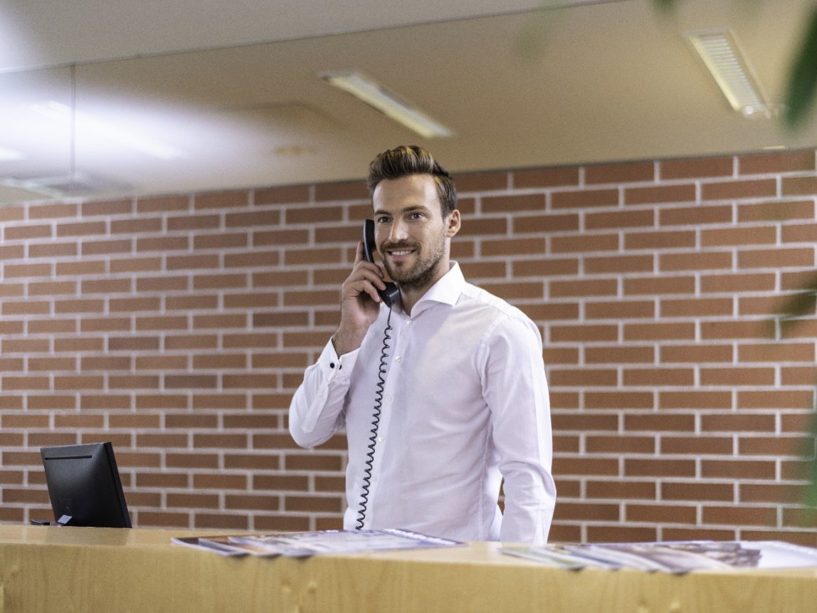 Smiling man standing in front of brick wall holding a telephone receiver